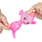 Pink glittery axolotl toy held by two hands on a white background