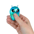 Hand holding a small blue glittery creature toy on a white background
