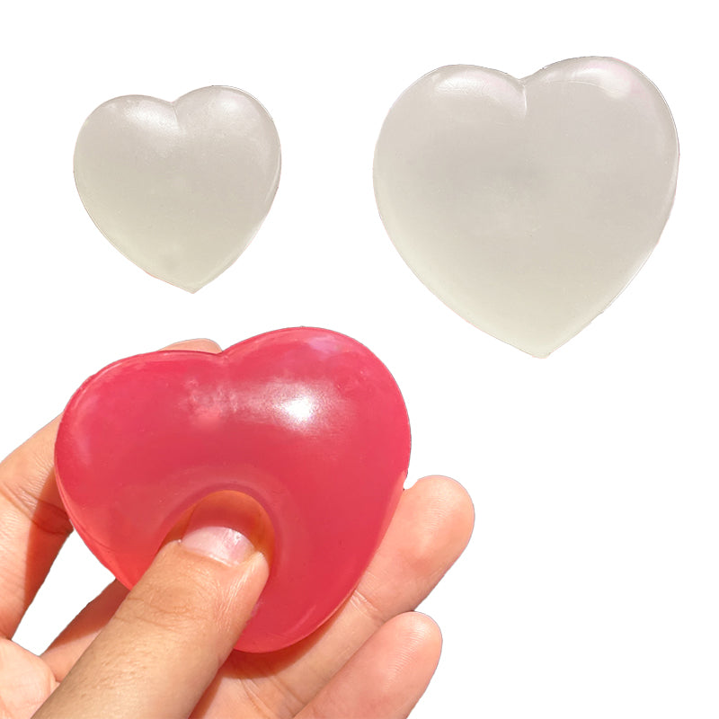 A translucent heart-shaped stress toy shown being squeezed by a hand, with two additional unpressed translucent heart toys floating above on a white background.