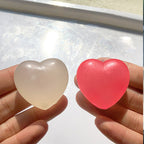 Two translucent heart-shaped items held between hands, one pale frosted white and one bright pink, against a light reflective background.