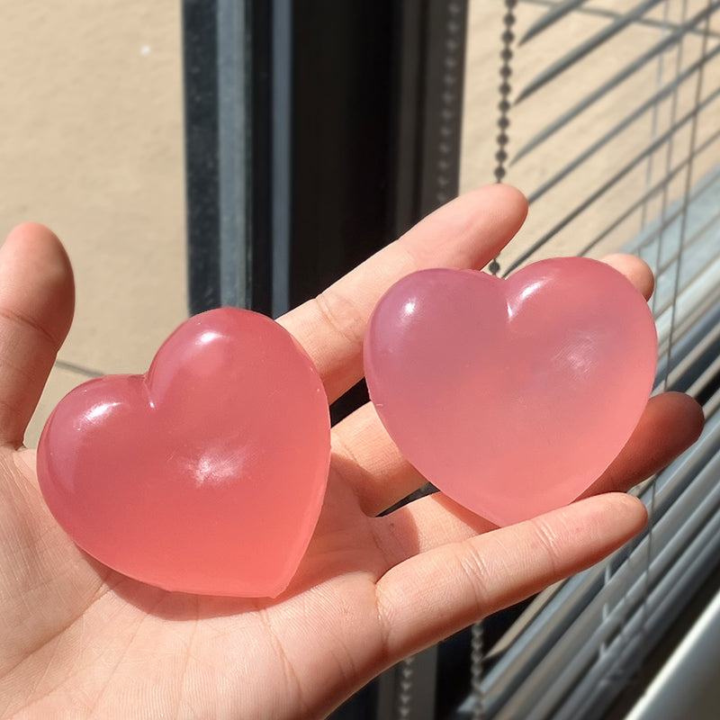 Two translucent pink heart-shaped objects held in a person's hand, photographed in bright natural light near window blinds.