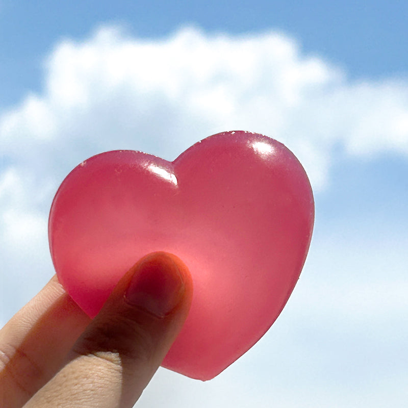 Heart-shaped pink object held against a blue sky with clouds