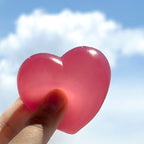 Heart-shaped pink object held against a blue sky with clouds