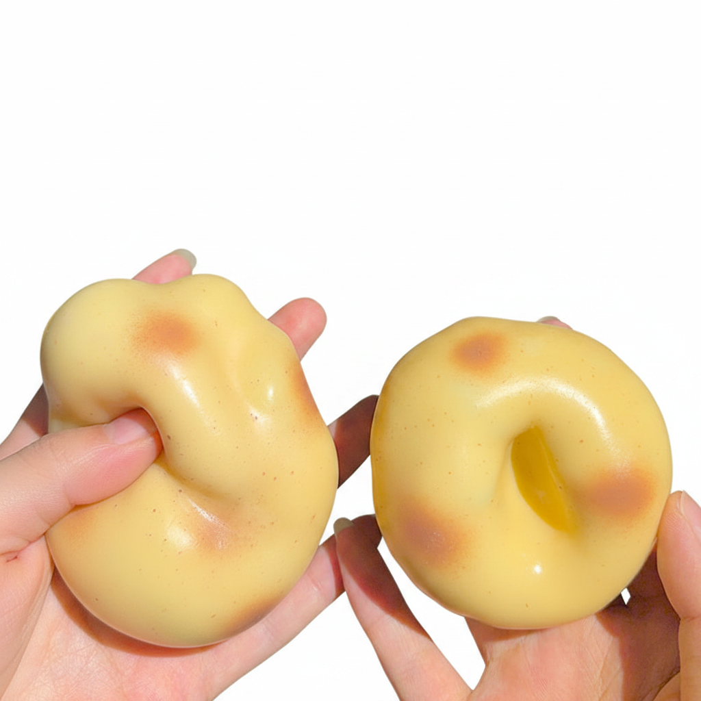 Two hands holding glossy golden potato squishy balls, one squeezed